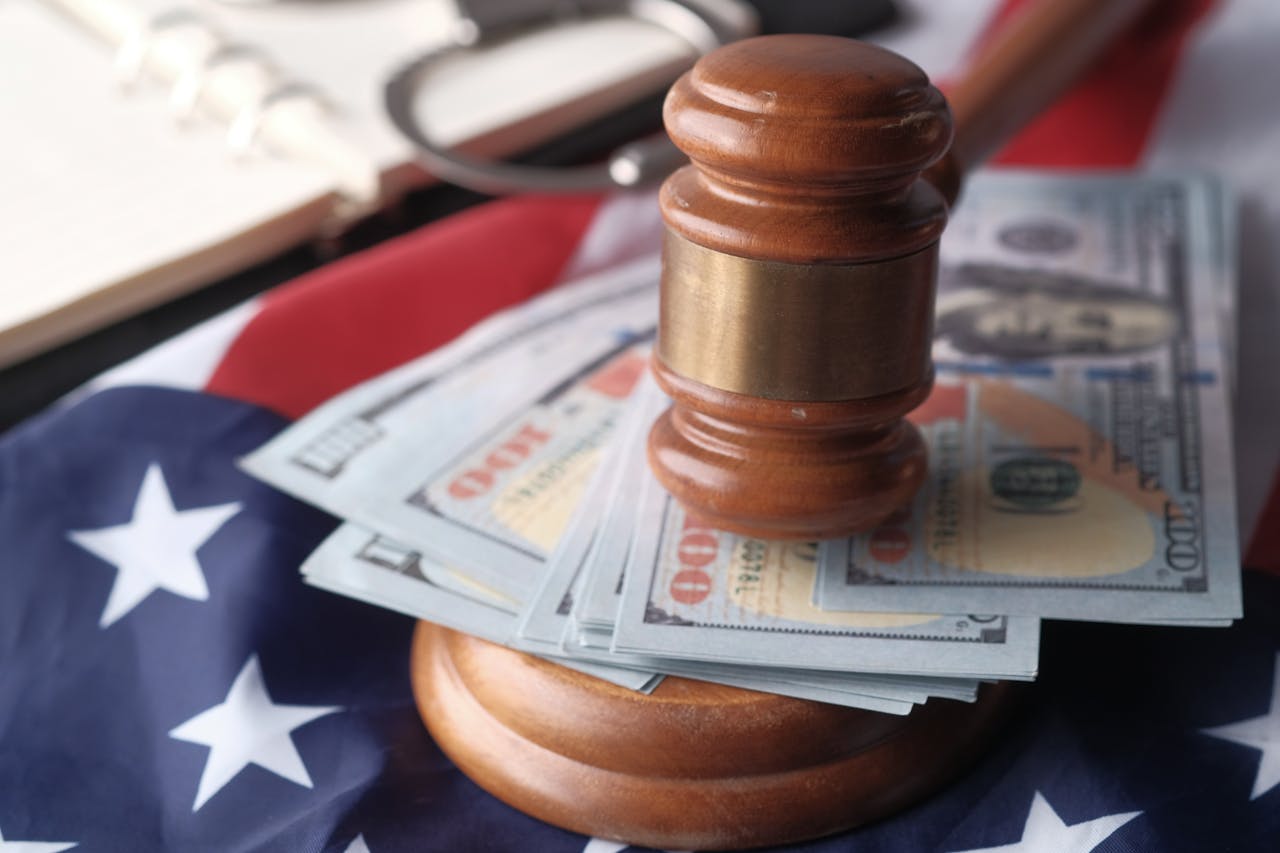 Close-up of a judge's gavel resting on US dollar bills and an American flag, symbolizing justice and finance.